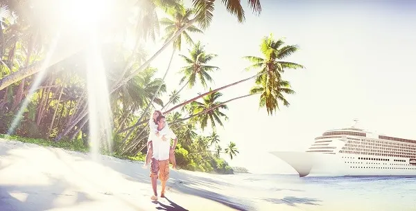 couple on white sandy beach with palm trees and a cruise ship in the background