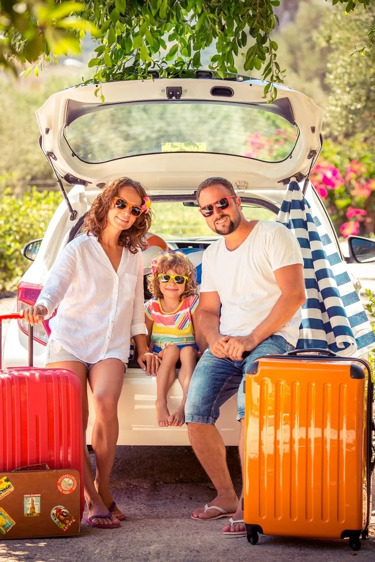 a family mother father and daughter with red and orange suitcases packing their white car for vacation