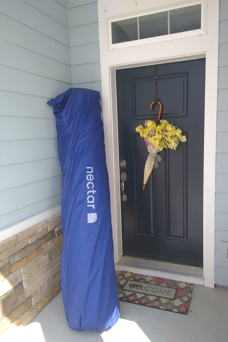 king size nectar mattress rolled in shipping packaging on front porch next to navy blue front door